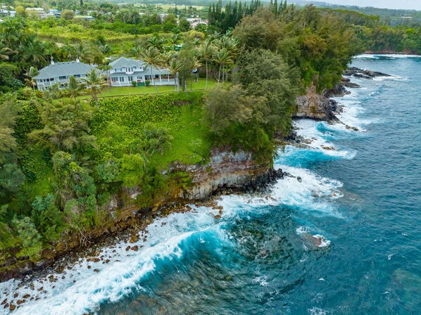 A coastal property with a large house surrounded by lush greenery and a rocky shoreline.