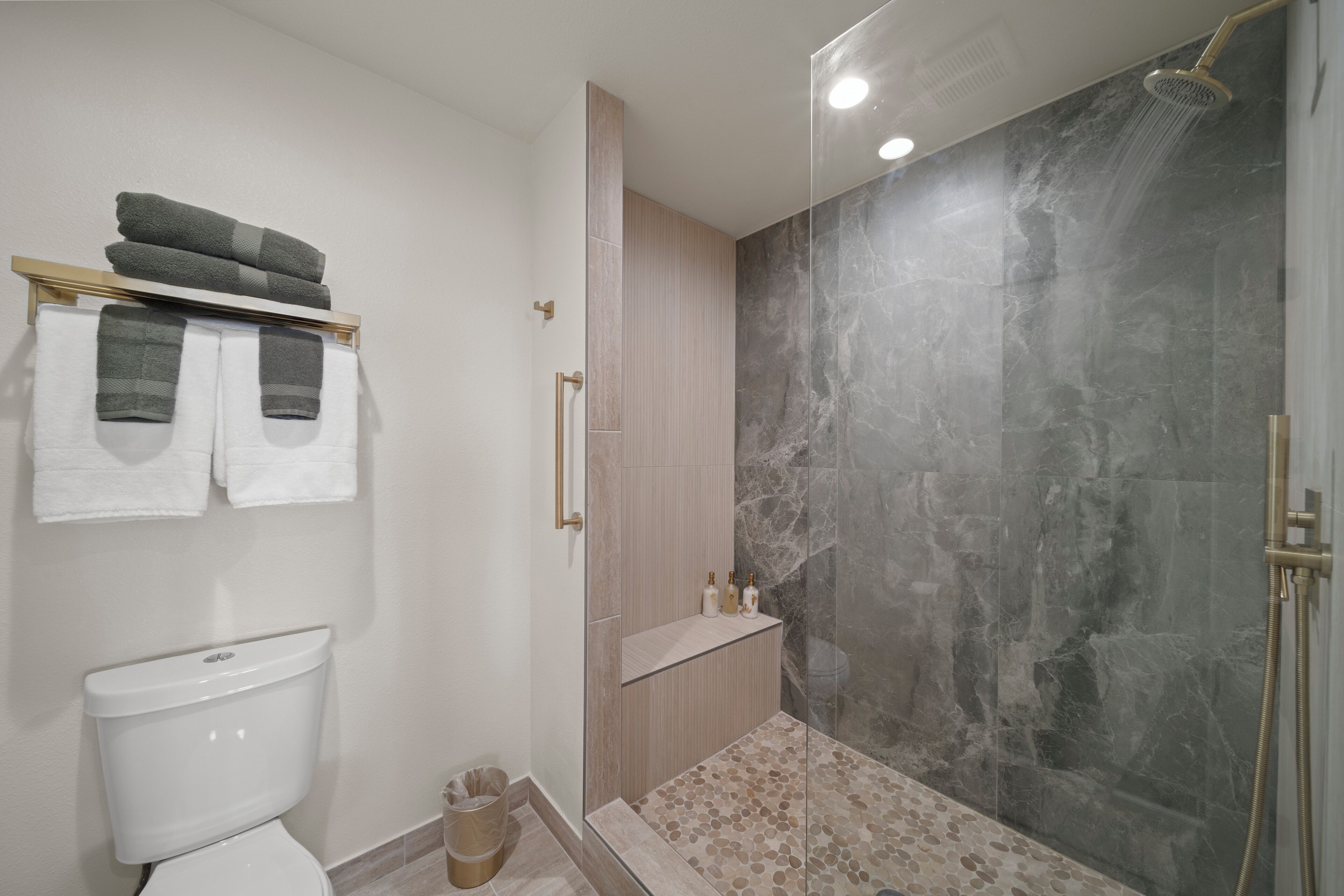 A modern bathroom with a toilet, a towel rack with towels, a glass shower enclosure, and a marble wall.