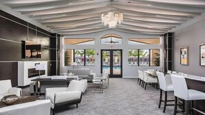 A modern hotel lobby with a high ceiling, a chandelier, a pool view, and a dining area with white furniture.