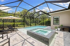 Una piscina exterior techada con sillas de descanso y una sombrilla, rodeada por una estructura de metal y paneles de vidrio.