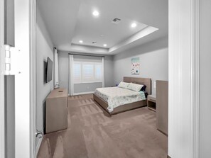 Un dormitorio con cama, mesitas de noche, televisión y ventana con persianas.