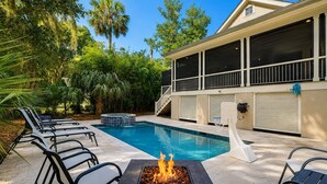 Une piscine avec des chaises longues, un foyer extérieur et un espace couvert offrant une vue sur la maison.