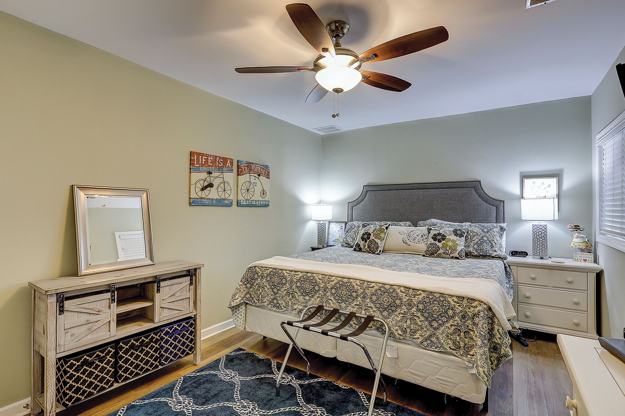A bedroom with a bed, bedside tables, a ceiling fan, a dresser, and wall decorations.