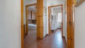 Un couloir avec des portes en bois et un sol carrelé qui mène à une chambre à coucher équipée d’un lit et d’une armoire.