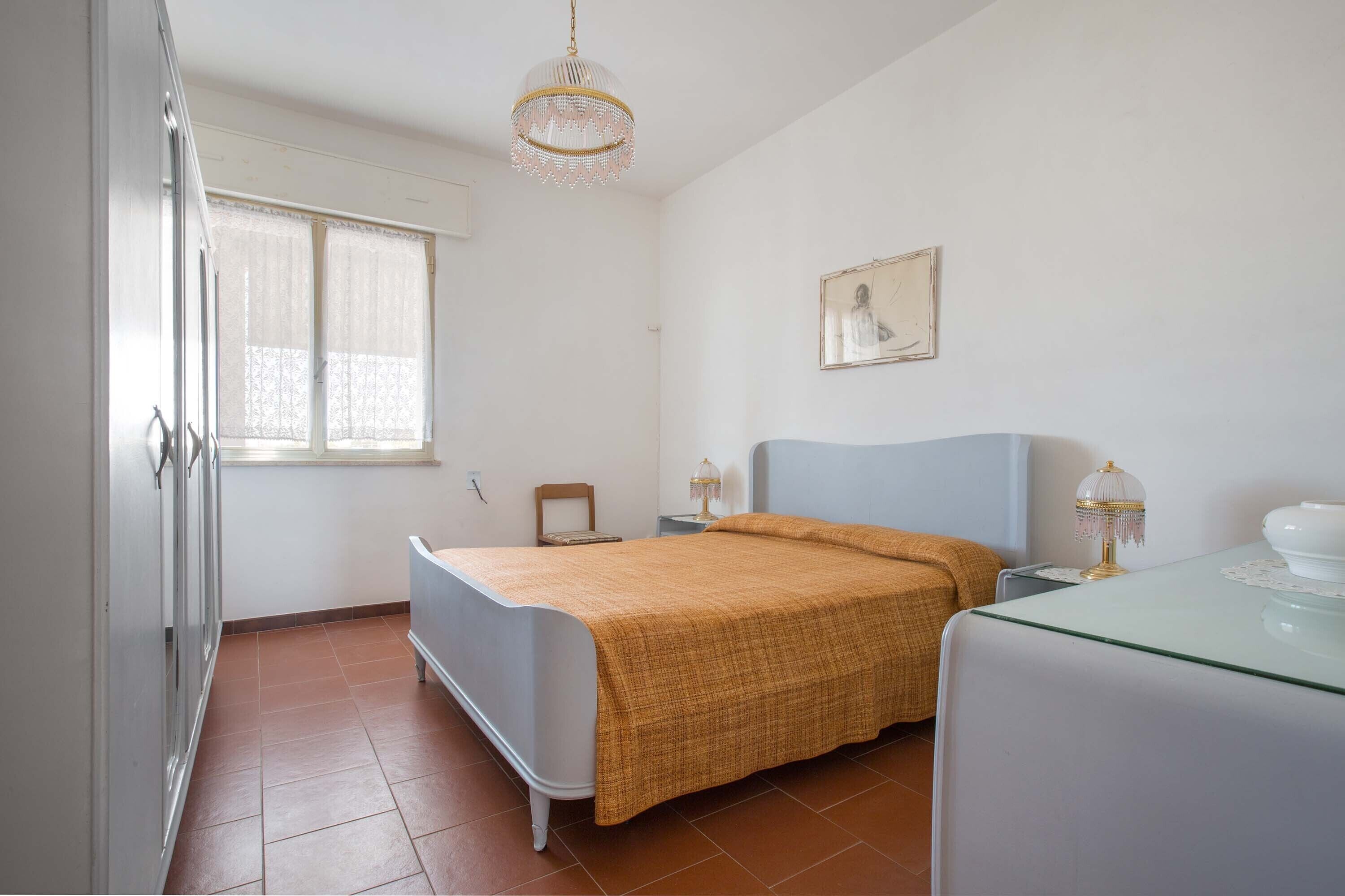 A bedroom with a bed, a nightstand, a lamp, a chair, and a window with curtains.
