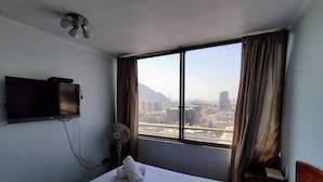Une chambre d’hôtel avec un lit, un téléviseur fixé au mur, une fenêtre avec des rideaux et une vue sur la ville.
