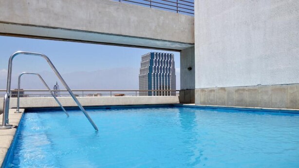 Une piscine avec un escalier en métal, des murs en béton et une vue sur un grand immeuble en arrière-plan.