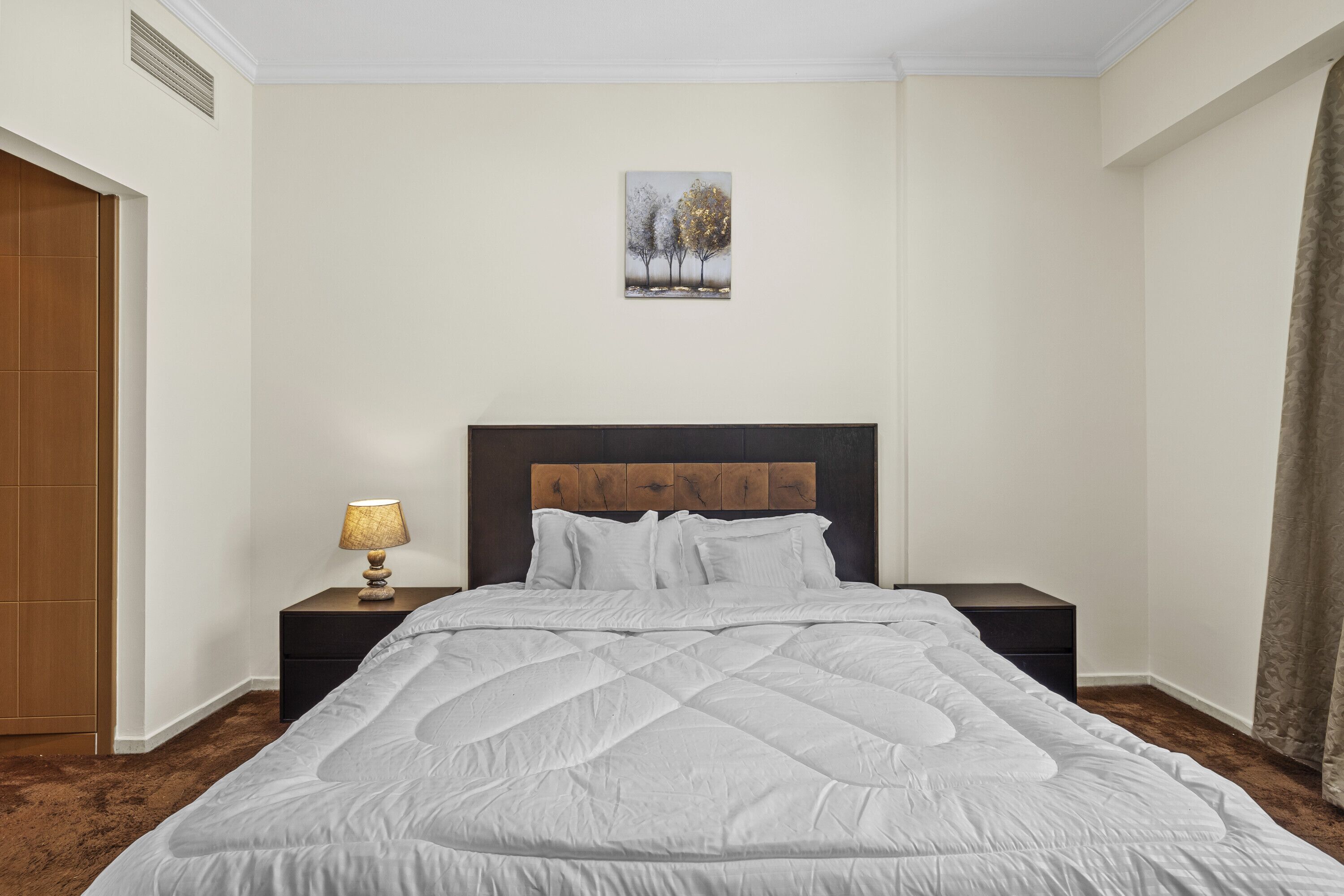 A neatly made bed with a quilted white duvet, a wooden headboard, and a small bedside table with a lamp.