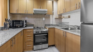 A kitchen with wooden cabinets, a stainless steel refrigerator, a microwave, a stove, and a sink. - Pure Living - Cozy Apartment With Balcony In Silicon Oasis (Dubai)
