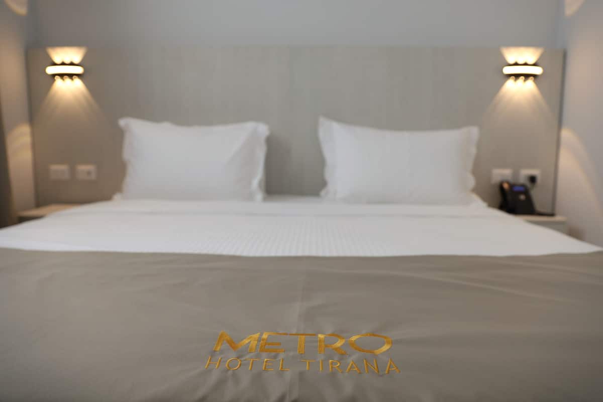 Quarto de hotel com uma cama, duas luminárias fixadas na parede e uma tomada visível.