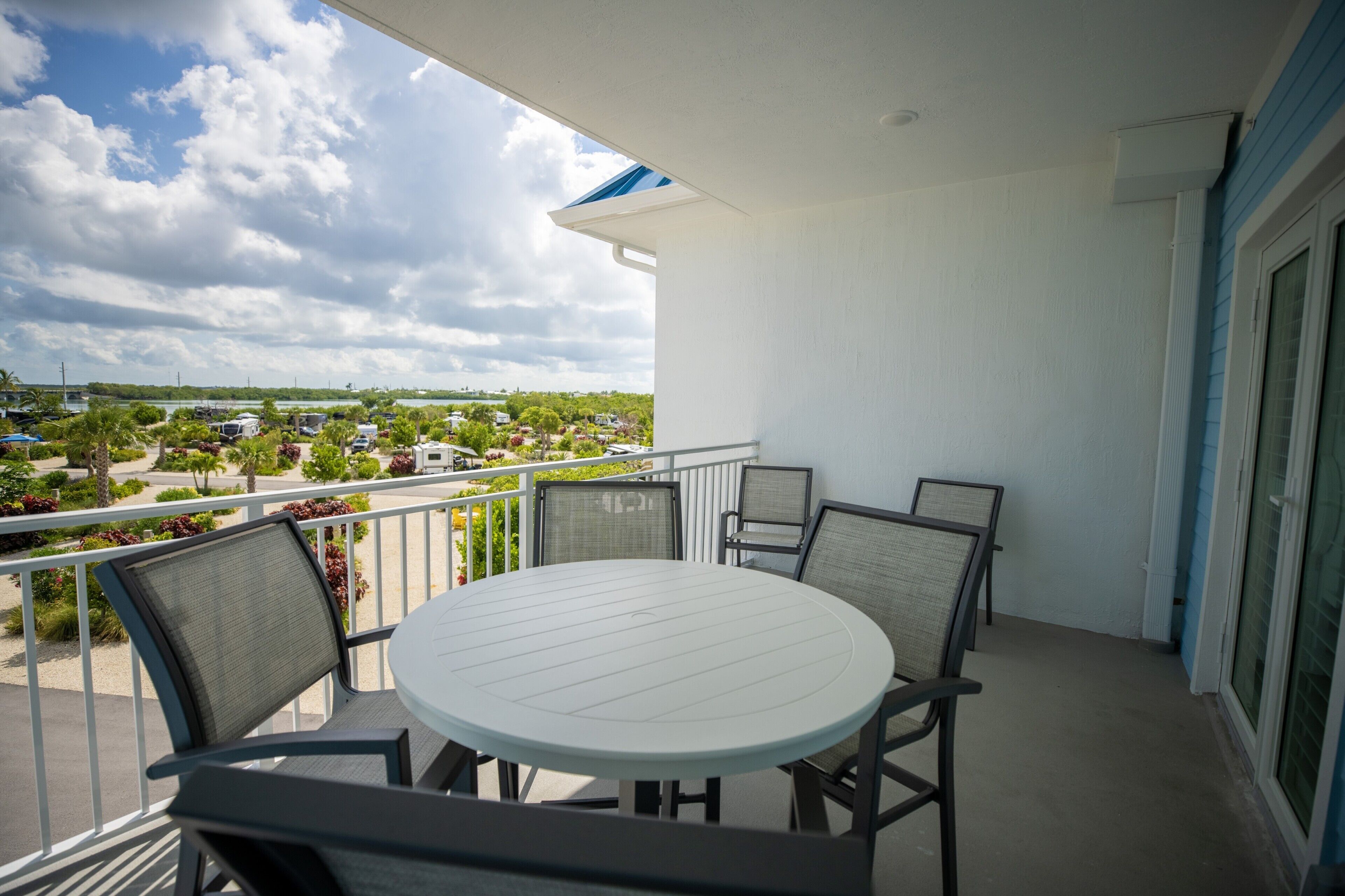 A balcony with a round table and chairs, overlooking a marina with boats and greenery.