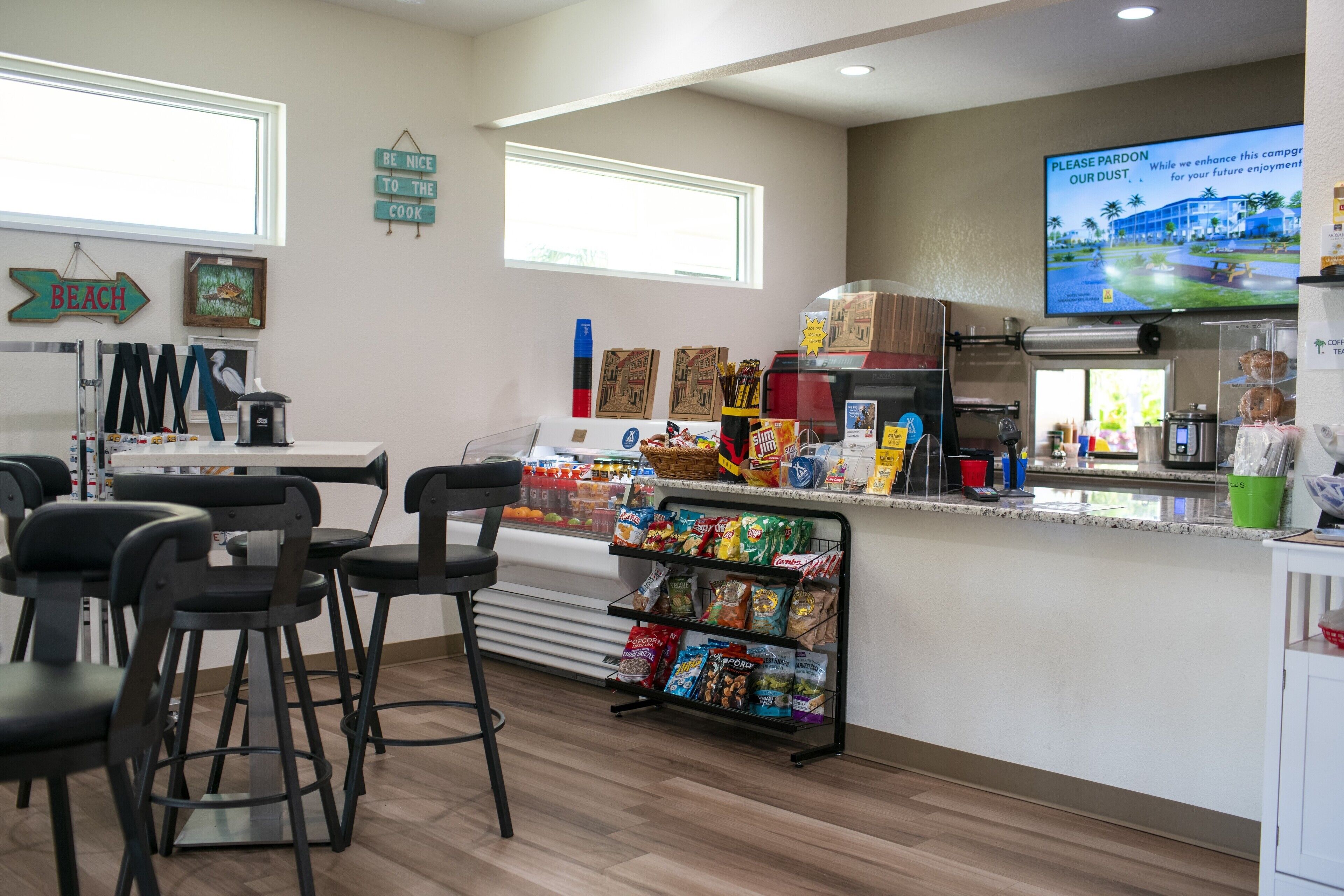 A kitchen area with a coffee machine, a snack bar stocked with chips and other snacks, and a television displaying a building.