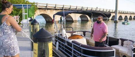 A boat docked at a pier with a covered seating area and a bridge in the background.