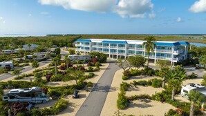 A resort with multiple RV parking, a central walkway, and a building with balconies overlooking a body of water. - Sugarloaf Key Hotel at KOA Resort (Summerland Key)