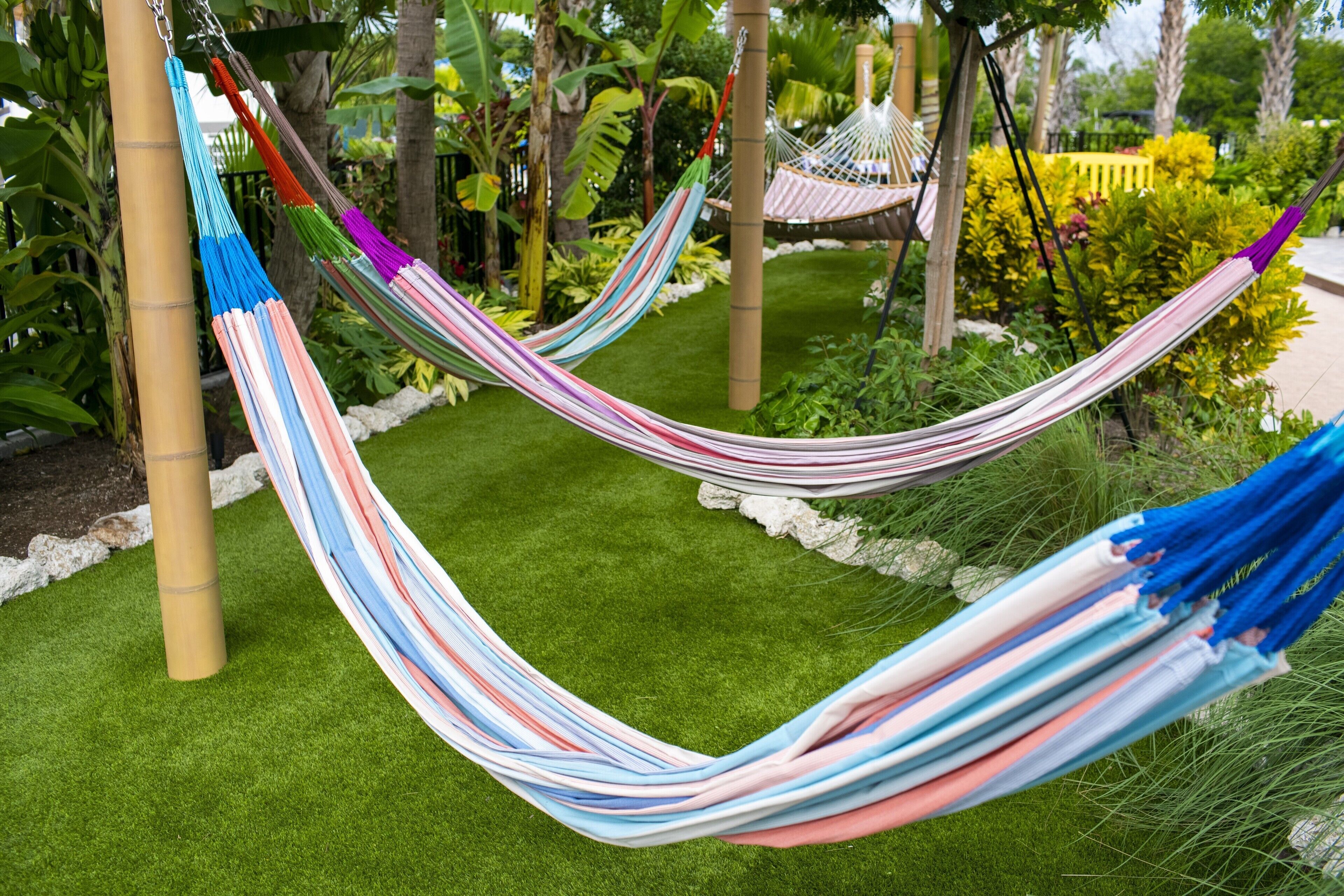 A hammock in a lush garden with green grass and various plants.