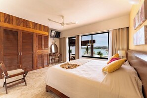 Une chambre d’hôtel avec un grand lit, un bureau, une chaise, un ventilateur de plafond et une vue sur l’océan.