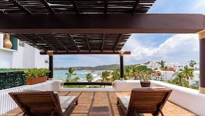 A covered outdoor seating area with a view of the ocean and hills.