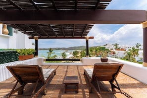 A covered outdoor seating area with a view of the ocean and hills.