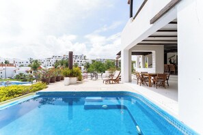 Une piscine sur le toit offrant une vue sur des bâtiments blancs, avec des meubles d’extérieur et des plantes en pot.