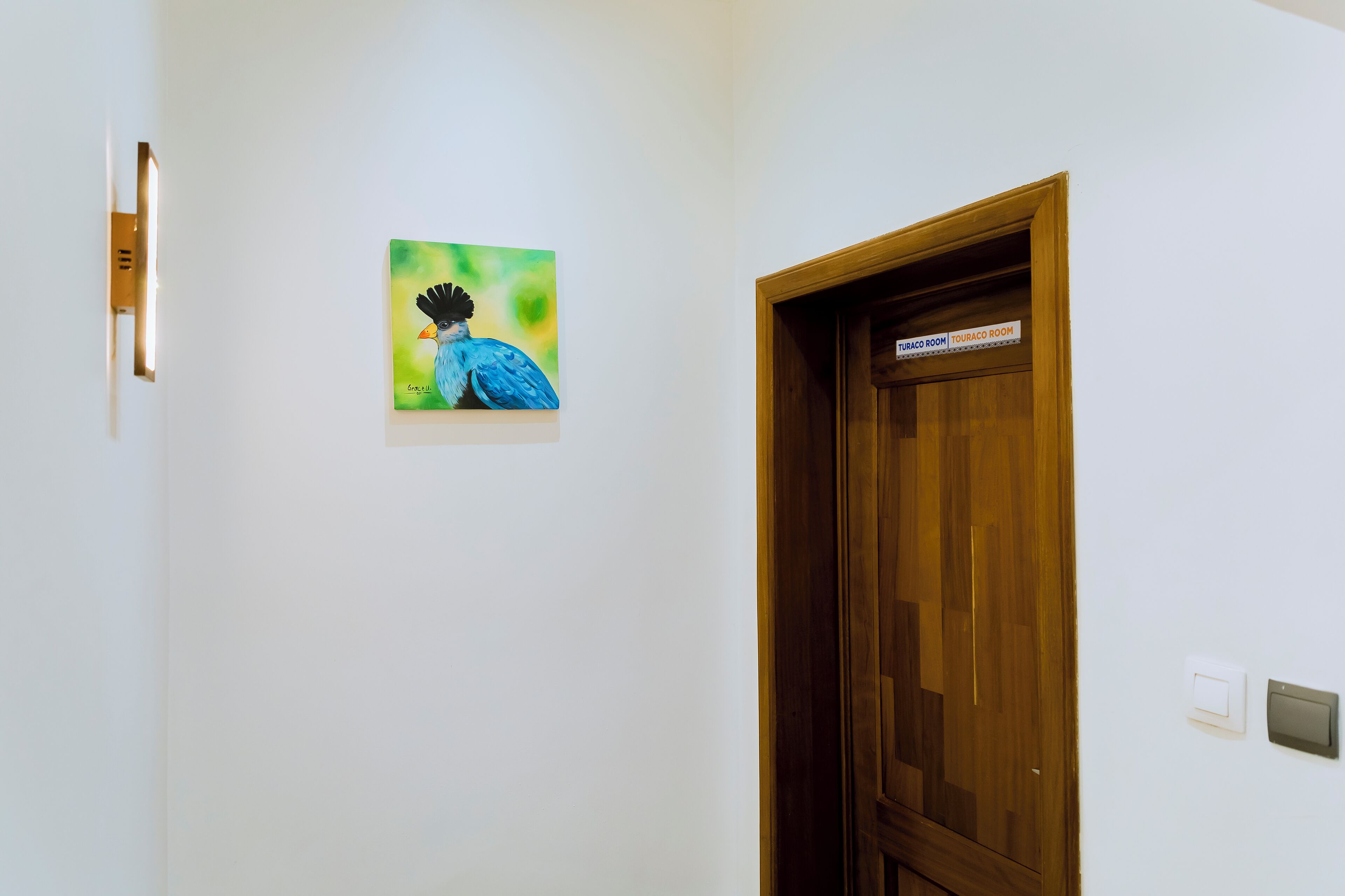 A wooden door with a sign indicating a room, a light switch, and a framed picture on the wall.