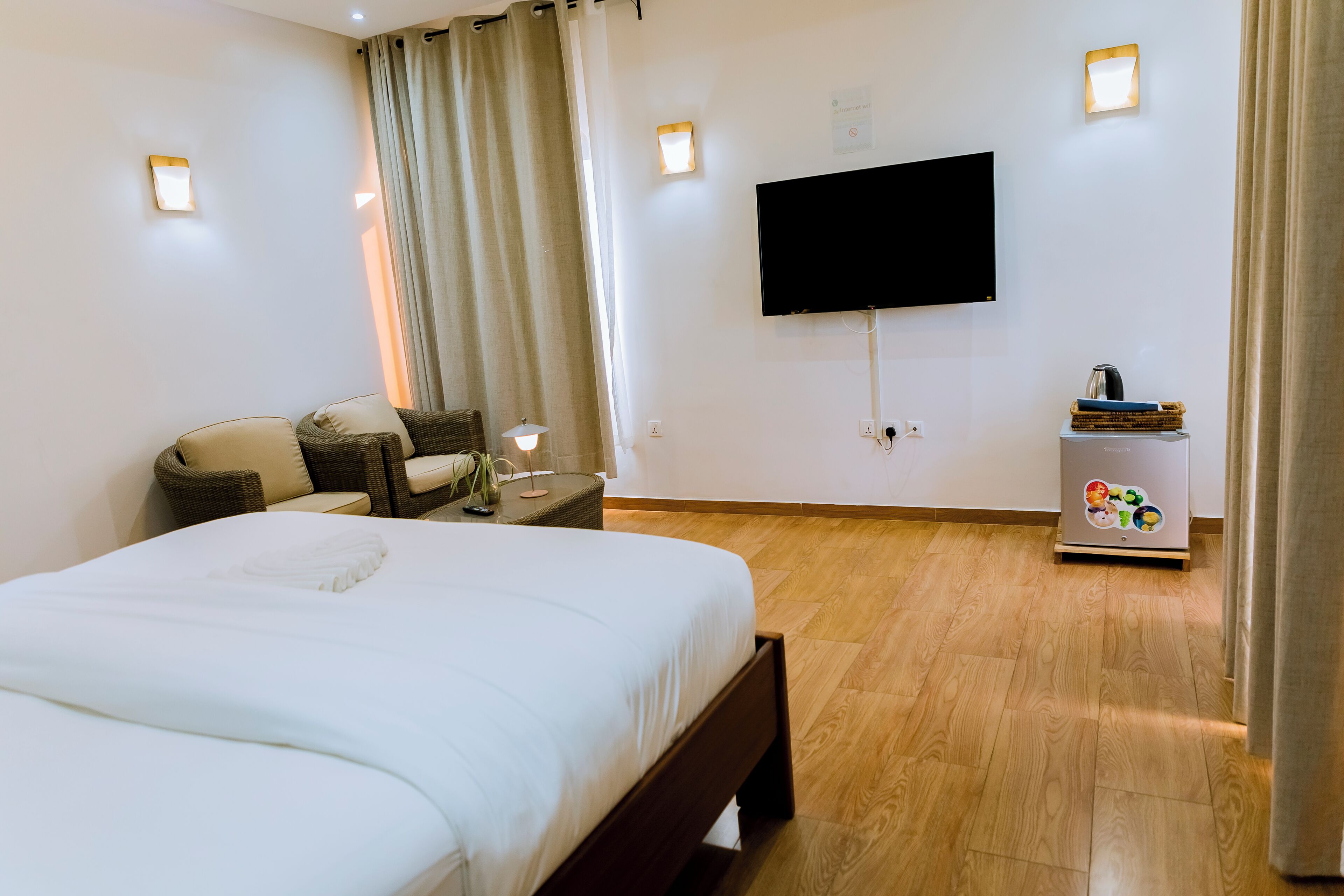 Habitación de hotel con una cama grande, un televisor montado en la pared, una mesita auxiliar pequeña y suelo de madera.