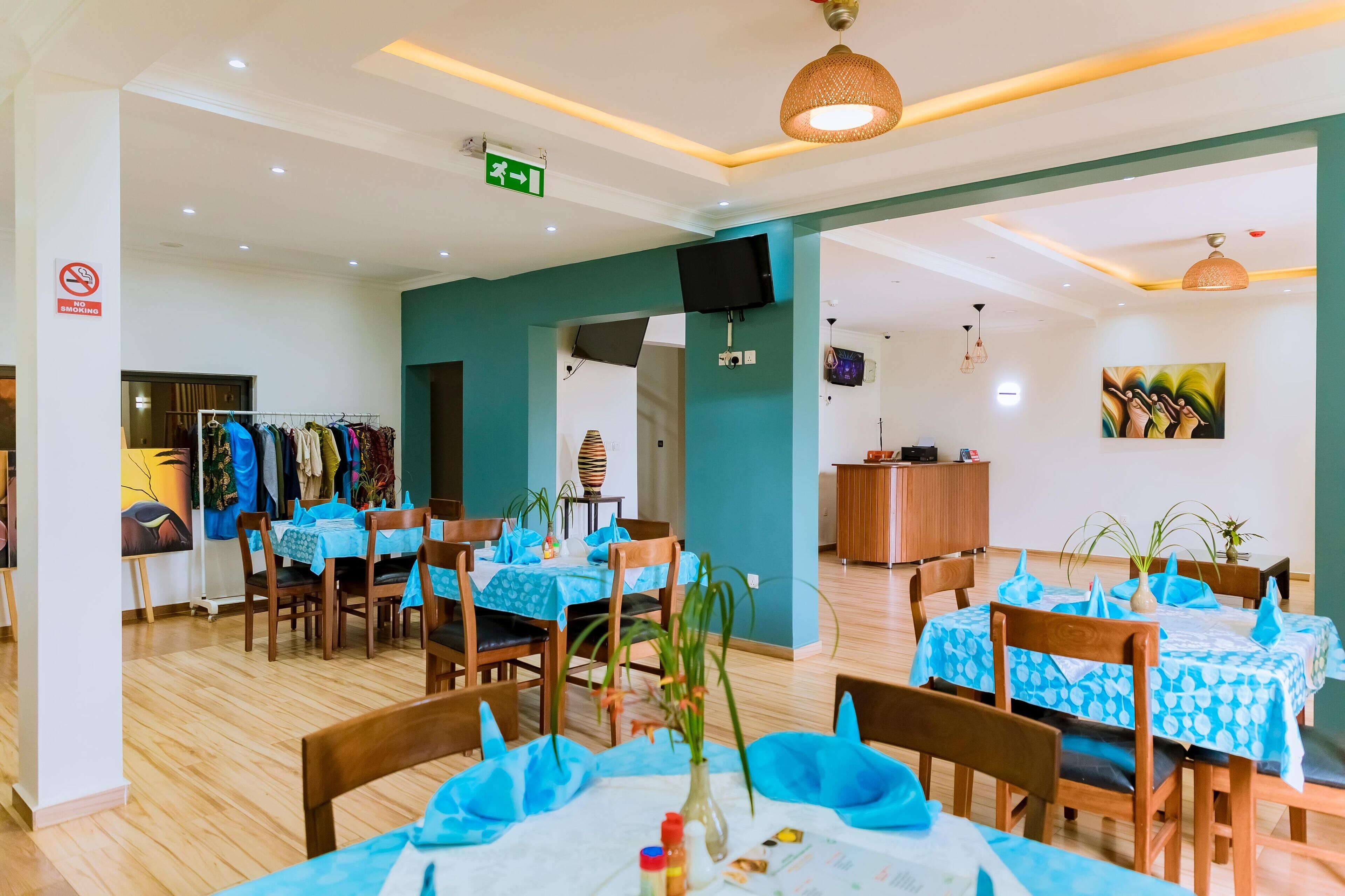 A dining area with tables covered in blue tablecloths, wooden chairs, and potted plants.