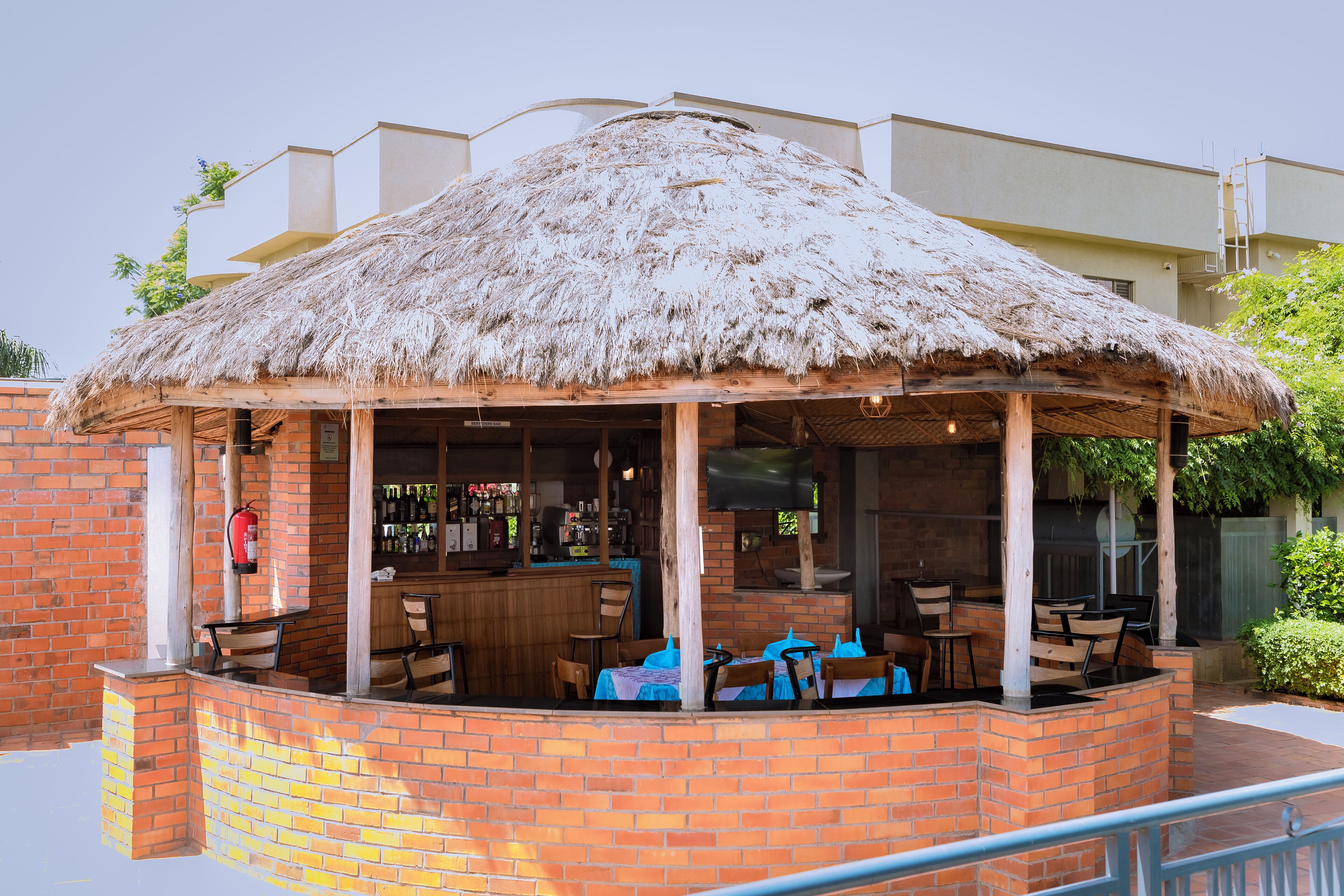 A covered outdoor seating area with brick walls, a thatched roof, and a bar with visible bottles.