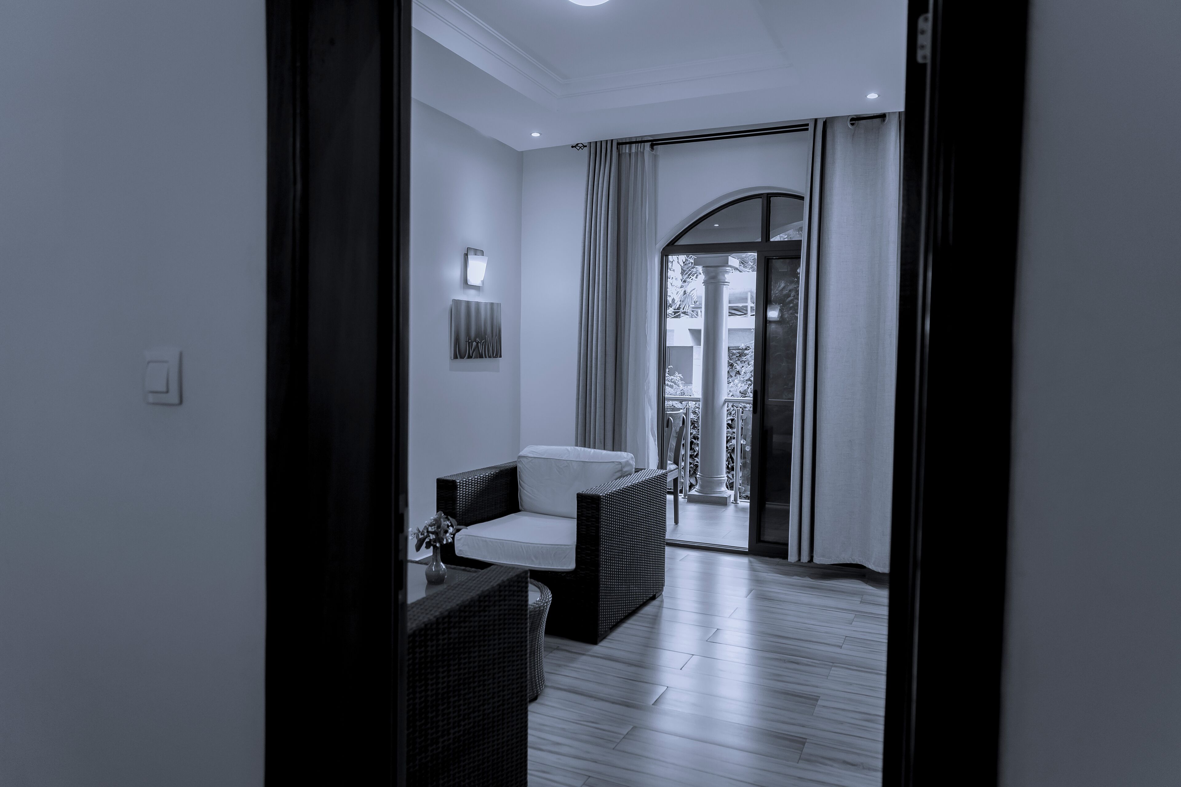 A modern room with a wicker sofa, a small table with a vase, and a view of an outdoor balcony with a glass door.