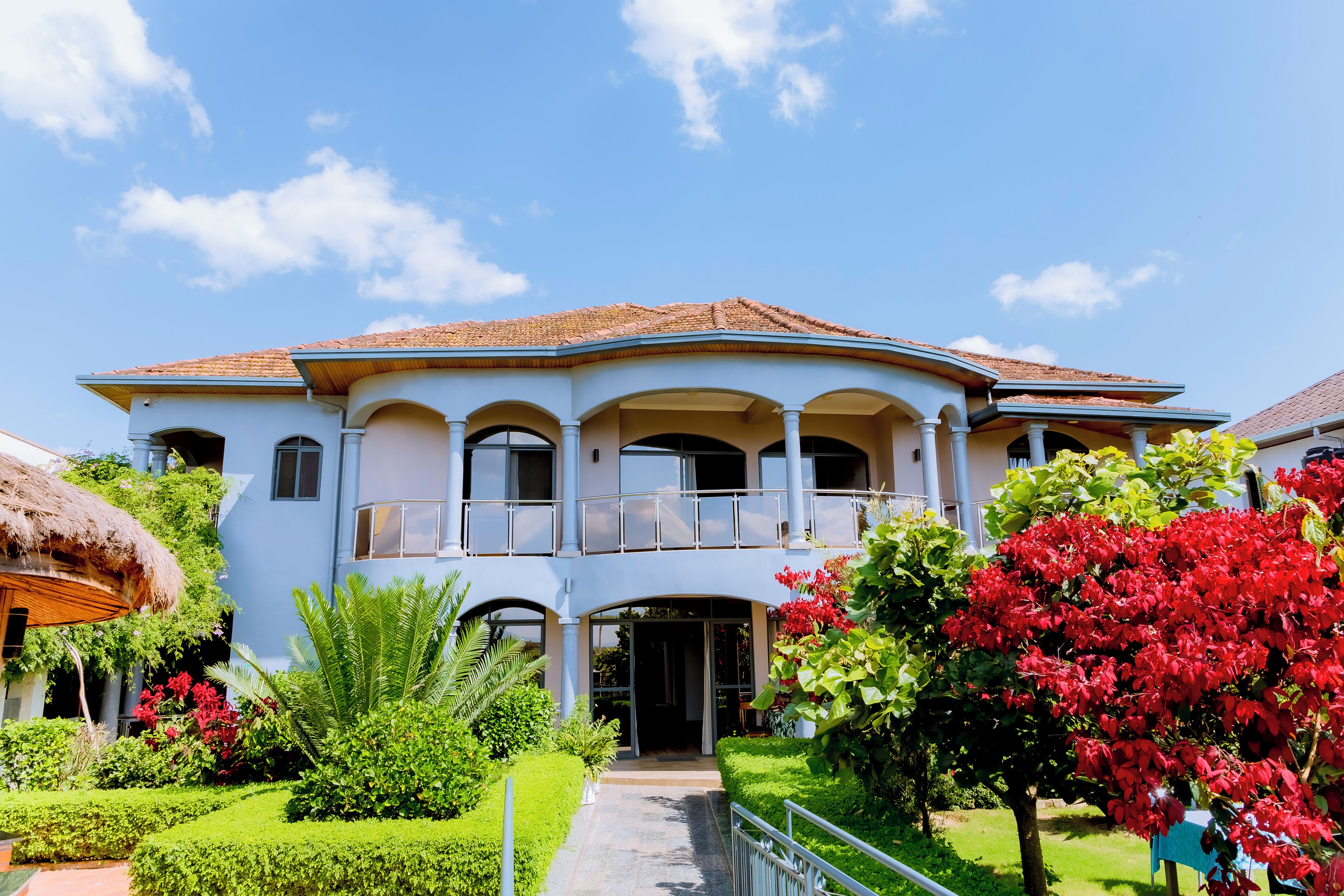 A two-story building with a balcony, surrounded by well-maintained gardens and a thatched-roof structure.