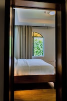 Quarto com cama, janela com vista para vegetação e luminária no teto.