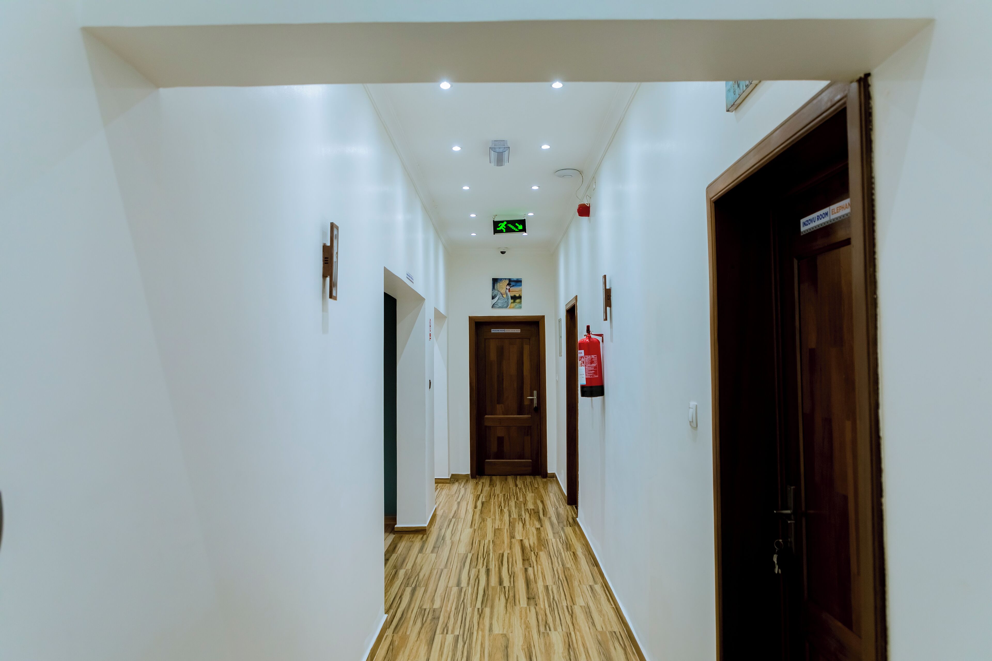 A hotel hallway with white walls, wooden flooring, and doors on both sides.
