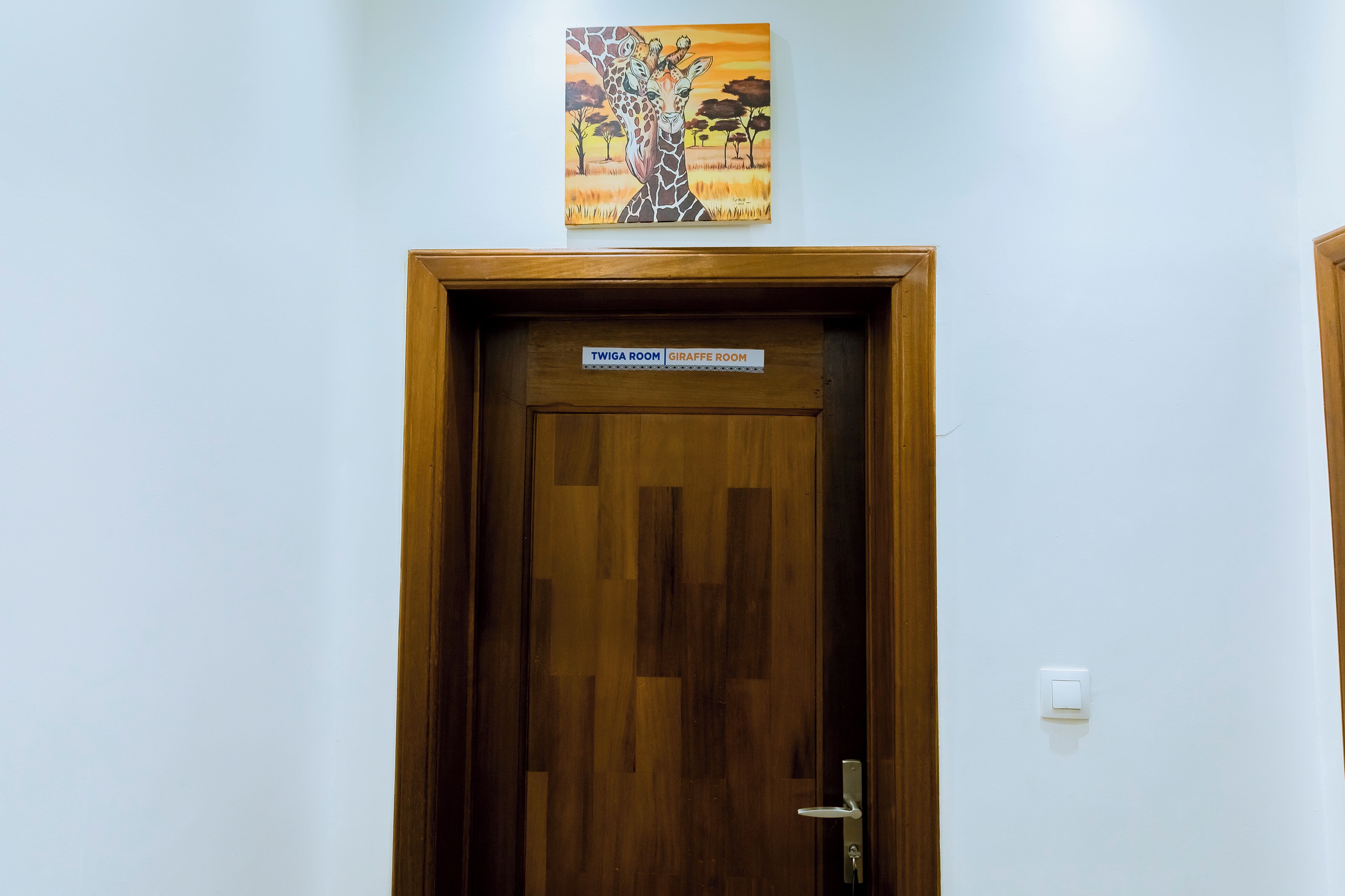 A wooden door with a sign reading "TWIGA ROOM GIRAFFE ROOM" and a painting of giraffes above it.