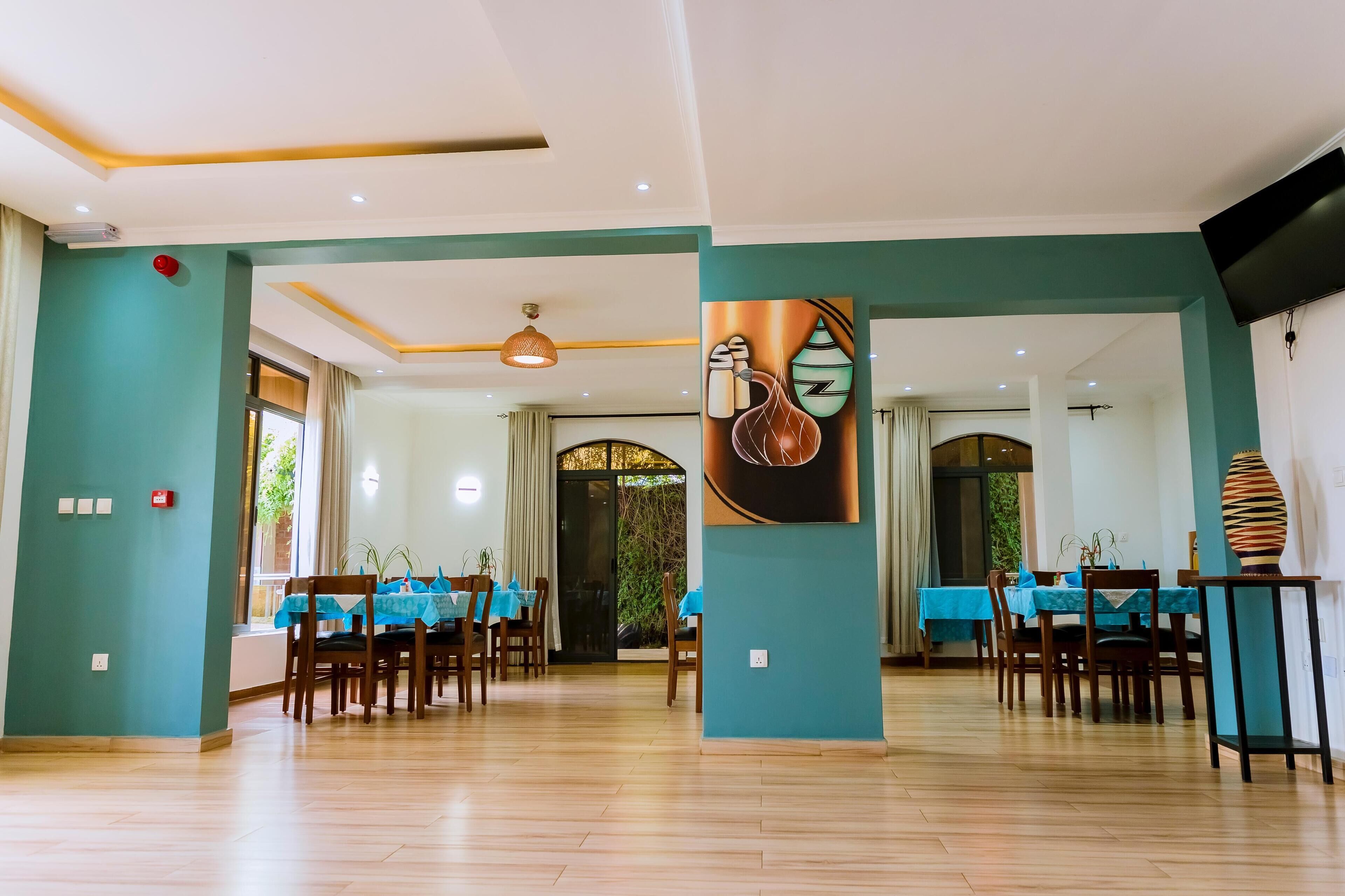 A spacious dining area with blue tablecloths and wooden chairs, a large painting on the wall, and a modern ceiling design.