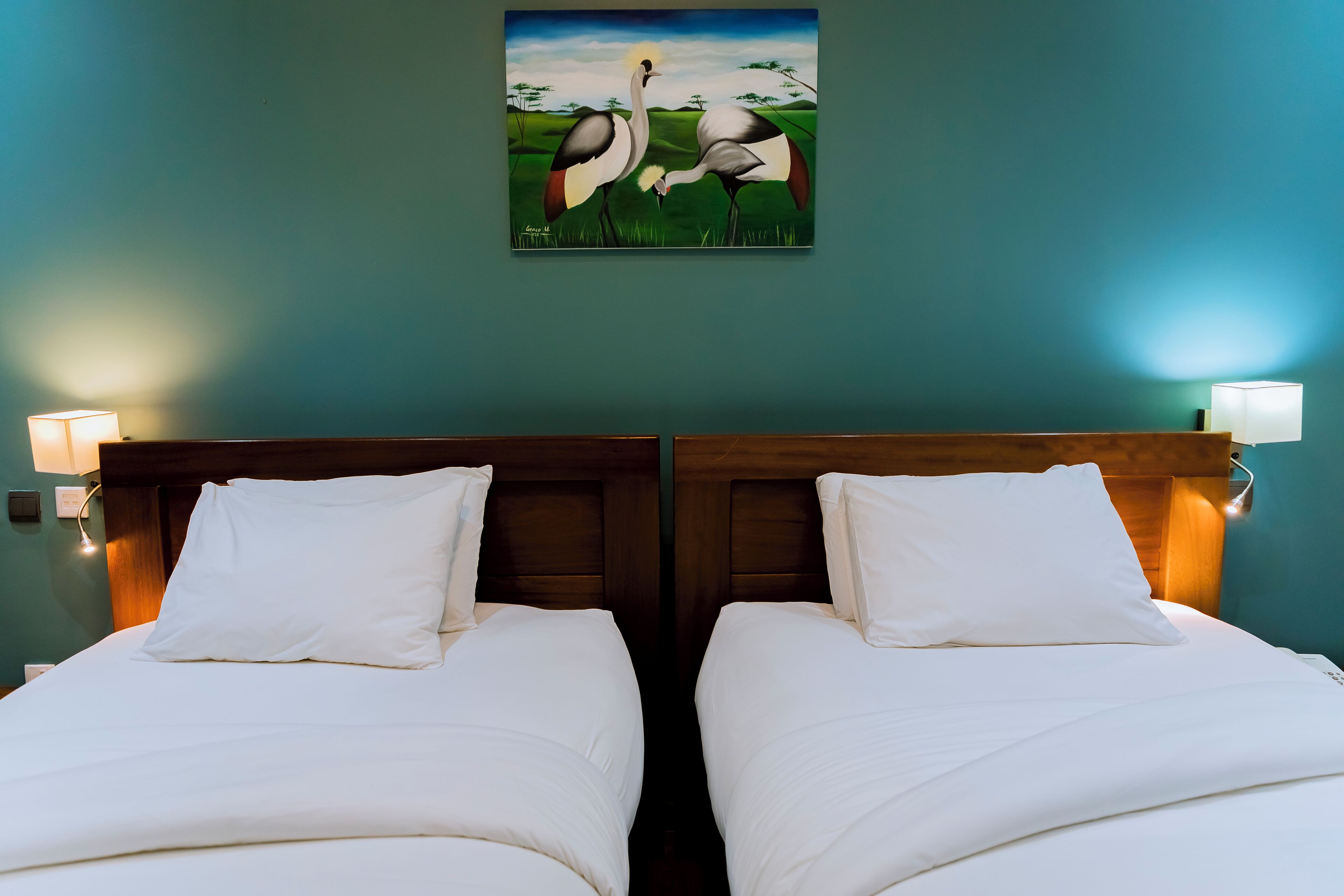 A room with two beds, a wooden headboard, and a painting of birds on the wall.