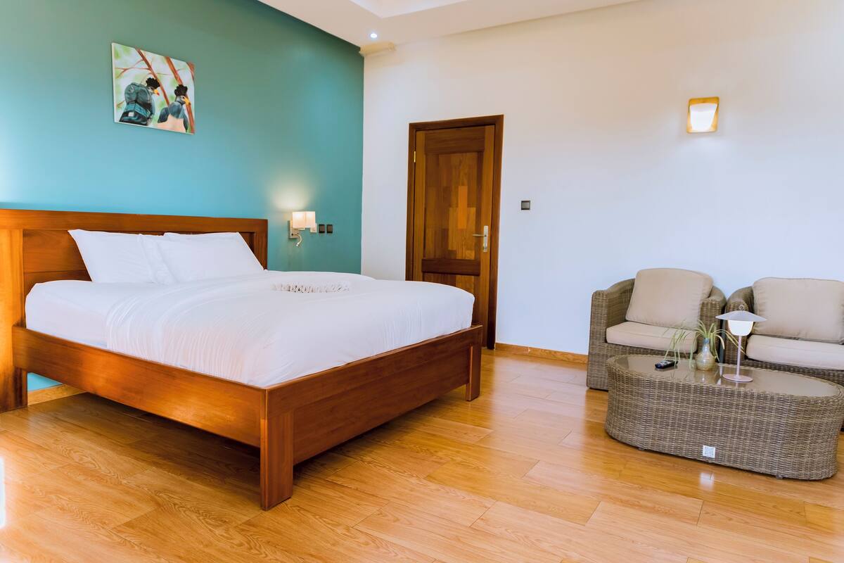 A bedroom with a wooden bed, a wicker sofa, and a small table with a lamp.