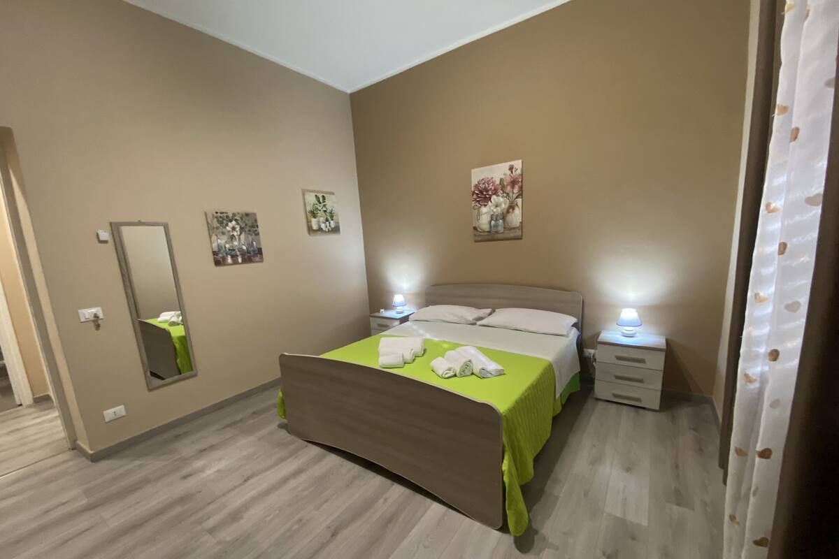 A bedroom with a bed, bedside tables, a mirror, and wall art.