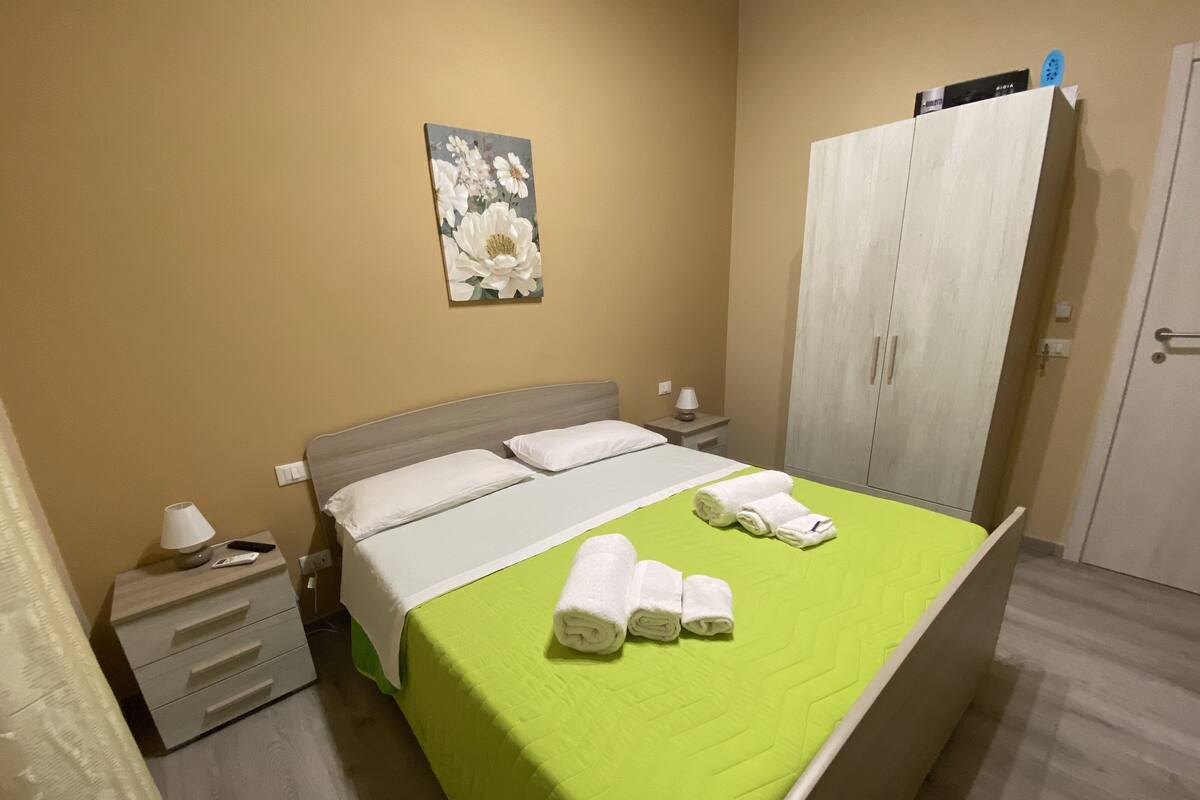 A hotel room with a bed, a nightstand, a lamp, a wardrobe, and a painting on the wall.