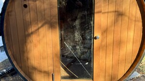 A wooden barrel-shaped structure with a door, a small window, and a metal handle. - Raleigh Retreat with Sauna+Hot Tub (Garner)