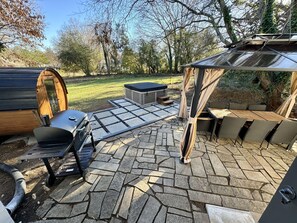 Un'area patio con pavimento in pietra, vasca idromassaggio, barbecue e zona salotto coperta.