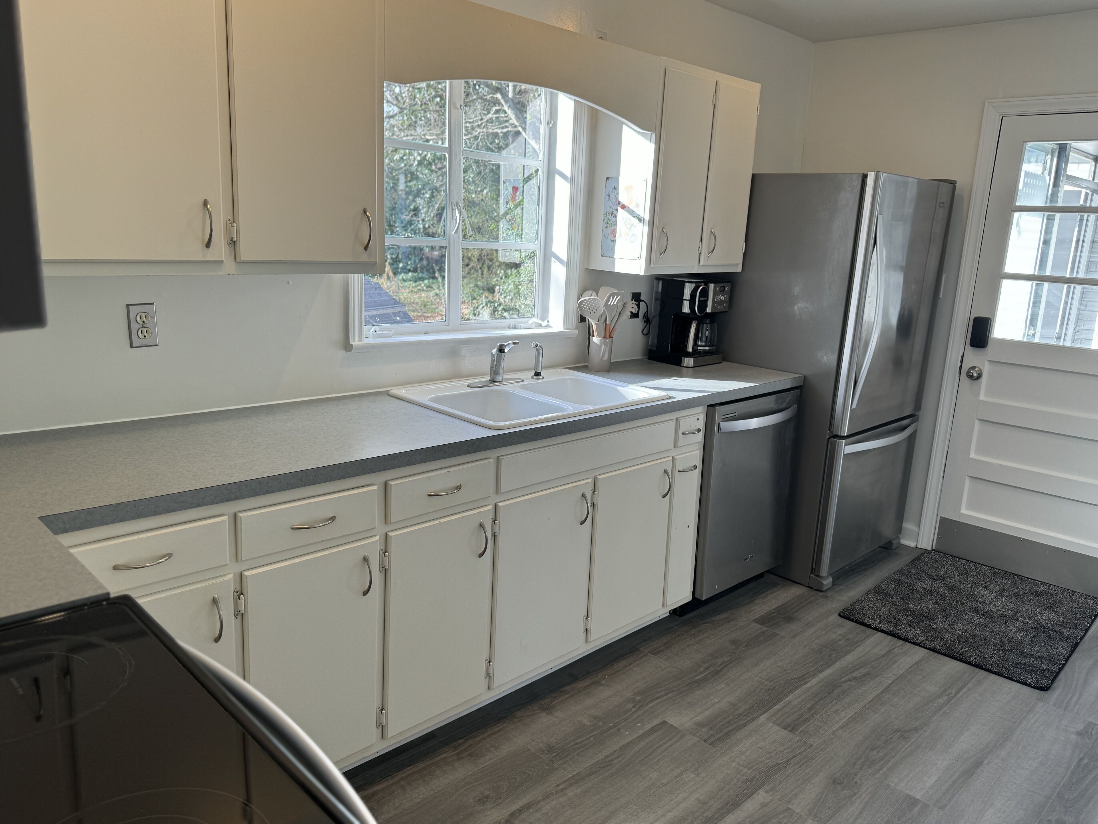 A modern kitchen with white cabinets, a stainless steel refrigerator, a coffee maker, and a window providing natural light.