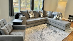 A modern living room with a sectional sofa, a small side table, and a patterned rug. - Raleigh Retreat with Sauna+Hot Tub (Garner)