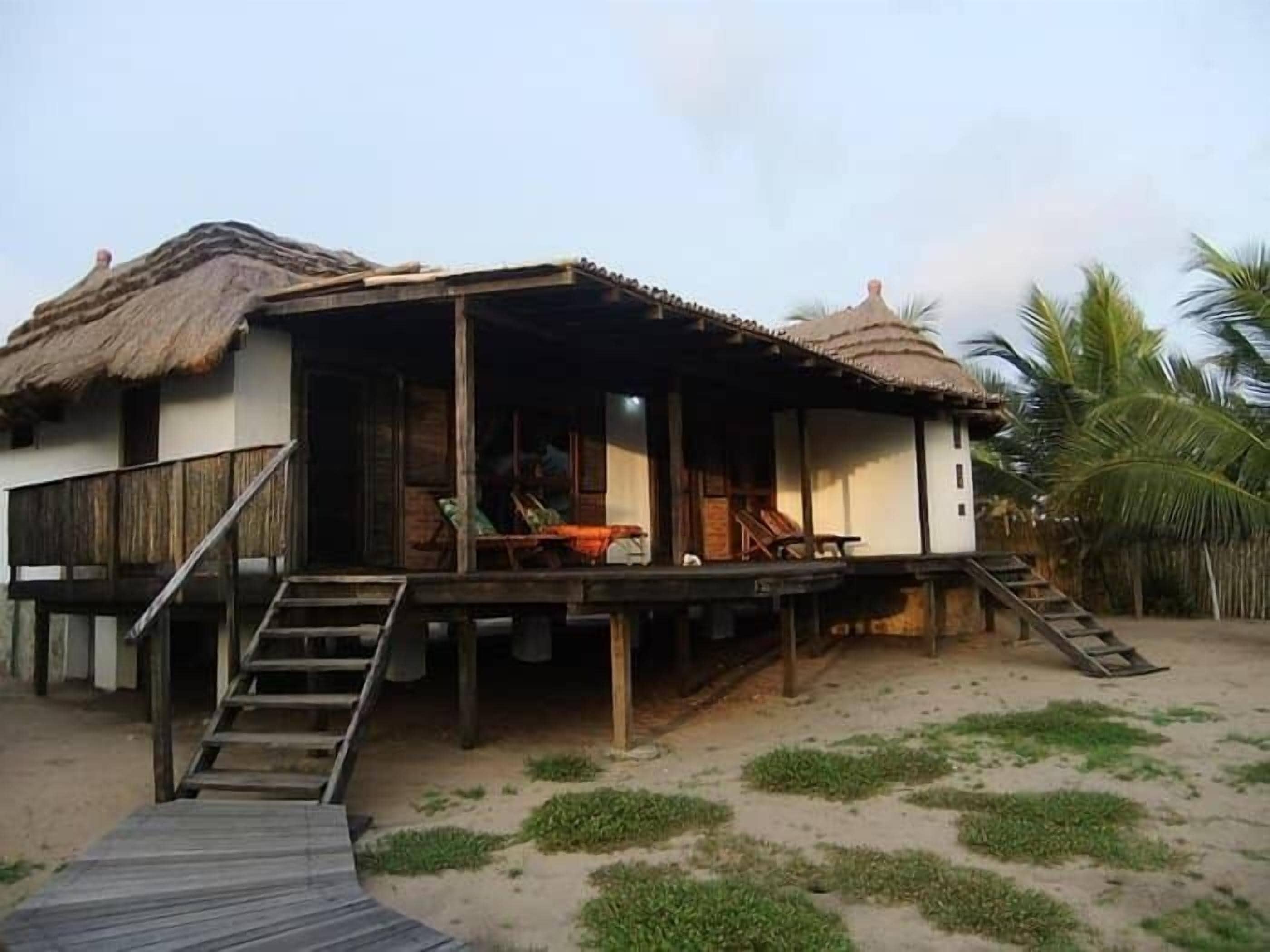 A beachfront bungalow with a wooden deck and a thatched roof.