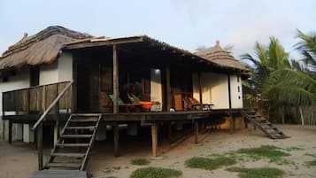 A beachfront bungalow with a wooden deck and a thatched roof.