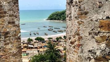 Vista através de antigas muralhas de pedra, com uma praia, barcos e uma pequena cidade.