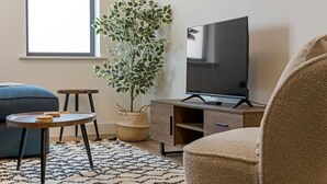 En stue med et stort fladskærms-tv, en blå sofa, et lille rundt bord med småkager, en flettet kurv og en potteplante.
