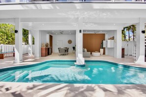Ein moderner Poolbereich mit klarem Pool, weißen Säulen und einer überdachten Sitzgelegenheit.