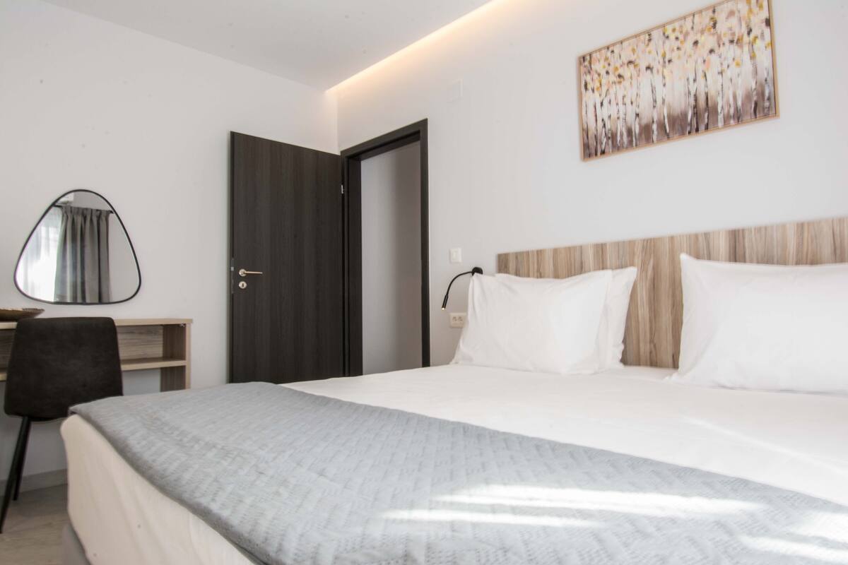Ein modernes Hotelzimmer mit einem großen Bett, einem Schreibtisch mit Stuhl und einer Tür zu einem weiteren Raum.