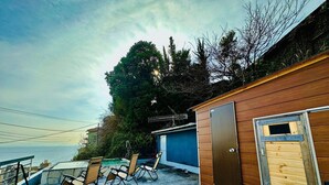 Una terraza de madera con sillas exteriores, una piscina pequeña y un edificio con puerta y ventana.