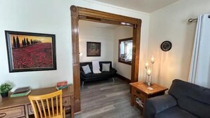 A cozy living room with a wooden-framed doorway, a black sofa, a wooden table with candles, and a painting of a field. - Kg Bd Full Condo steps to hospitals & Capitol 1-70 (Topeka)