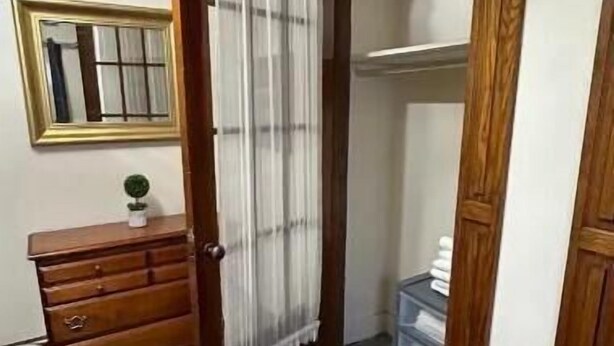 A bedroom with a wooden wardrobe, a bedside table with a lamp, a small plant, and a mirror on the wall. - Kg Bd Full Condo steps to hospitals & Capitol 1-70 (Topeka)
